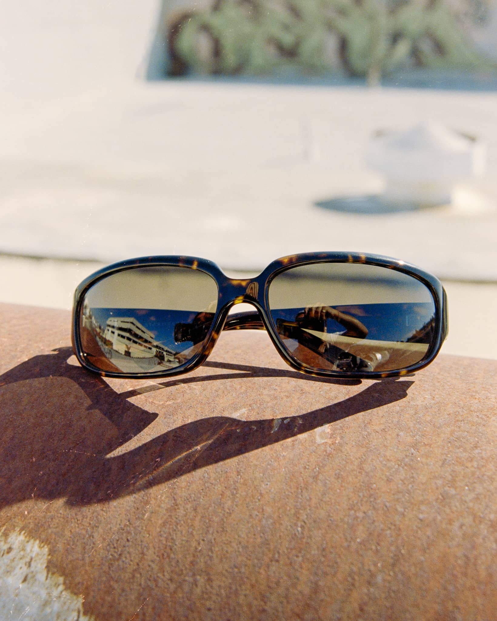 Oversized square sunglasses with a tortoiseshell frame and mirrored lenses, resting on a textured brown stone surface in bright sunlight.-The Stone Echo - Dark Tortoise Bio-6